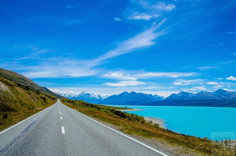 A road with a view of the ocean and mountains.