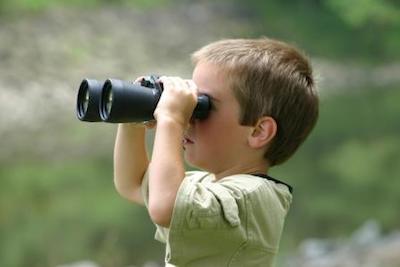 Child using binoculars outdoors near water.