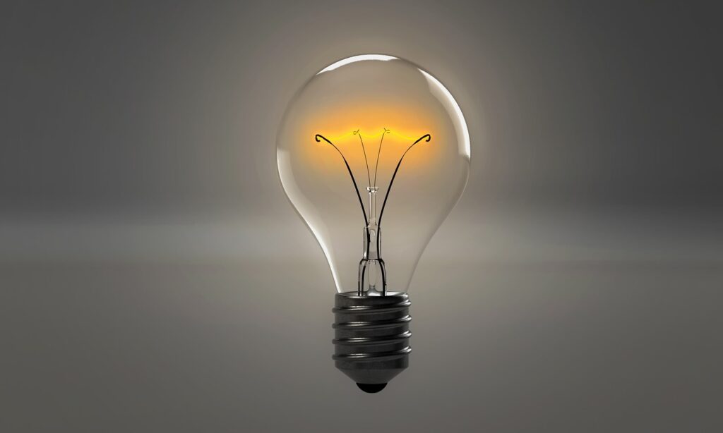 Lit incandescent light bulb on gray background.
