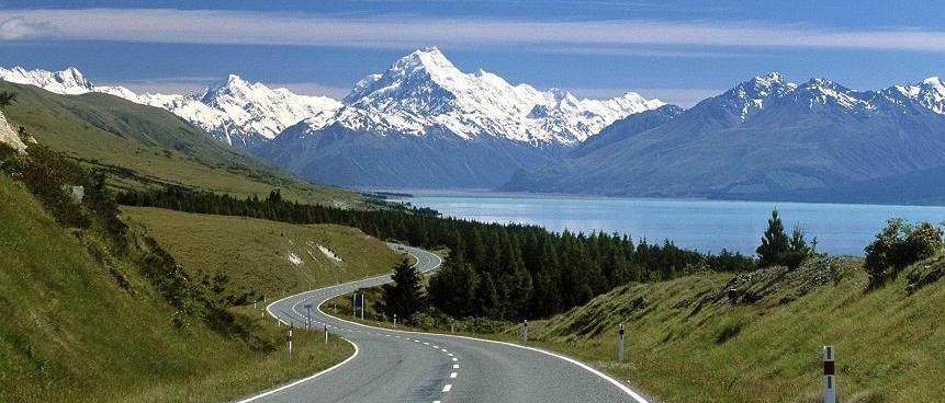 Winding road with snow-capped mountains and lake.