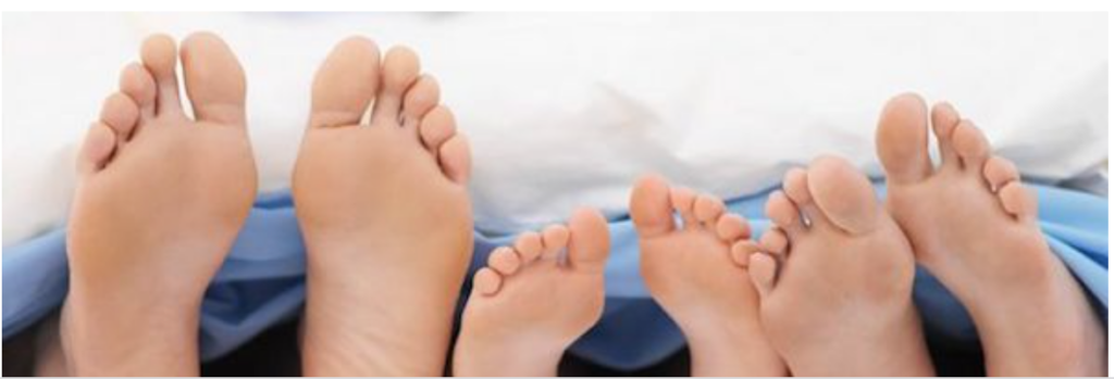 Four pairs of feet under a blanket.
