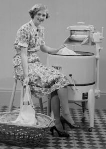 Woman using vintage washing machine, 1950s setting.