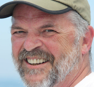 Man smiling, wearing a cap outdoors.