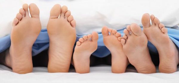 Four pairs of feet under a blanket.