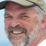 Smiling man wearing a hat outdoors.