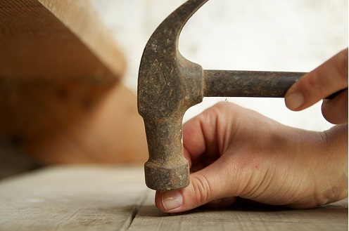 Hammer hitting nail on wooden surface.